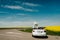 A newlywed wedding couple is driving a convertible retro car on a country straight road for their honeymoon. Way on spring field