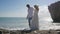 The newlyweds in embrace stand on the shore of ocean