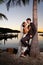 Newlyweds embracing under a palm tree at sunset