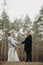 Newlyweds hold hands on background of pine tree forest