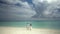 Newlyweds hold hands on a gorgeous white sand beach and turquoise water. In the background is a beautiful sky. Wedding on a tropic