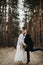 Newlyweds jump and kiss at forest path among pine trees