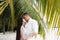 Newlyweds kiss in palm leaves on a white beach