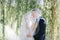 Newlyweds kiss under a veil on background willow