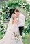 Newlyweds kiss at the wedding arch in the green garden