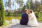 newlyweds kissing while sitting on wooden pier near lake at sunny summer day