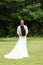 Newlyweds stand on a green lawn against the backdrop of a tropical forest