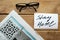 Newspaper, glasses and card with message Stay Home on wooden background.