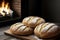 Next to a cozy fireplace, you\\\'ll find a trio of freshly baked loaves of bread resting on a wooden cutting board.