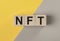 NFT acronym on wooden dices on yellow and gray background