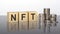 NFT - text on wooden cubes on a cold grey light background with stacks coins