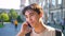 Nice asian boy is on the phone, smiling and talking, bright sun, urban view as background