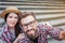 Nice bearded man and positive young woman sit on stairs and pose. He holds camera. They look at it. Tourists have rest.