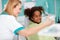 Nice black girl in dental chair showing teeth in mirror to dental assistant