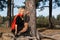 Nice blond hair woman sitting on the big roots of pine tree in coniferous autumn park.