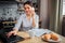 Nice cheerful woman sit at table and work at home. She typing on laptop keyboard and talk on phone. Her breakfast stand