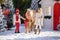 Nice children and adorable pony with festive wreath near the small wooden house and snow-covered trees. New Year and Christmas tim