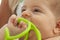 Nice closeup portrait of cute blond baby with brown eyes biting in a green plastic teether. Close up image