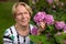 A nice elderly woman is posing in front of beautiful pink flowers