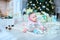 Nice female baby lying on floor on blanket with present near twinkling Christmas tree.