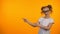 Nice girl in eyeglasses pointing at orange background, education opportunities