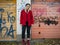 Nice girl in a knitted hat, a red jacket and red boots stands near the gate of the garage with graffiti