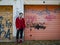 Nice girl in a knitted hat, a red jacket and red boots stands near the gate of the garage with graffiti