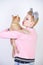 Nice kind woman with a short haircut and fur ears in sports clothes and jeans is holding her beloved pet on a white background in