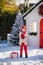 Nice little boy with red hat and green glasses and his big present near the Christmas tree