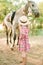 A nice little girl with light curly hair in a vintage plaid dress and a straw hat and a gray horse. Horses a