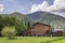 Nice new two-storied air- conditioned wooden house cottage behind stone brick fence on grassy meadow on green wooded mountains