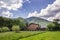 Nice new two-storied air- conditioned wooden house cottage behind stone brick fence on grassy meadow on green wooded mountains ba