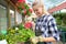 Nice positive flower seller holding  water can and watering flowers while being involved in work