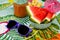 Nice shot of watermelon wedges, carrot juice, tiny umbrellas and a sunglass on a colorful tablecloth