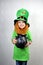 Nice smiling small girl with decorative red beard, green clover leaf on her cheek and leprechaun hat, holds cast iron pot, full of