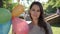 Nice young woman with braces on the teeth smiles and holds balloons in hand on background green trees