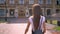 Nice young woman walks along in park in daytime in summer, turns head, building on background