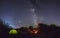 Night camping. Couple tourists have a rest at a campfire near illuminated tent under amazing night sky