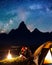 Night camping. Happy couple hikers sitting and kissing near a campfire and tent under the stars and Milky way