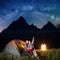 Night camping. Happy couple tourists sitting near tent and fire and enjoying incredibly beautiful starry sky, Milky way