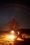 Night camping in mountains. Female hiker resting near campfire, tourist tent under starry sky