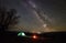 Night camping in the mountains. Hikers having a rest in tourist tent under starry sky near campfire