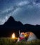 Night camping. Pair of backpackers sitting near tent and fire and enjoying incredibly beautiful starry sky, Milky way