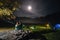 Night camping. Romantic couple tourists have a rest near illuminated tent under amazing night sky with moon. mist creeps over the