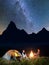 Night camping. Romantic pair sitting near campfire and tent under incredibly beautiful starry sky and Milky way