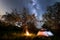 Night camping. tourist tent near campfire under trees and beautiful starry sky and milky way