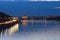 Night city landscape. Illuminated Pedestrian bridge over Dnipro River, silhouettes of buildings in