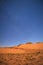 Night falls on the orange dunes of the desert under the moonlight and a deep, blue, starry sky.