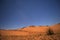 Night falls on the orange dunes of the desert under the moonlight and a deep, blue, starry sky.