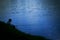 Night fishing, a dark silhouette of a fisherman with a fishing rod on a background of dark blue water